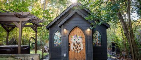 Une structure en bois dotée d’une porte sculptée en forme de hibou, d’un banc en bois et d’un chemin pavé de pierres.
