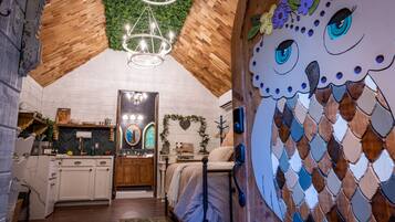 A cozy room with a wooden ceiling, a bed, a dresser, and a wall with a mosaic owl design.