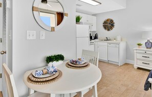 A modern kitchen with white cabinets, a microwave, and a stove. There's a dining area with a round table and chairs, and a decorative wall piece.