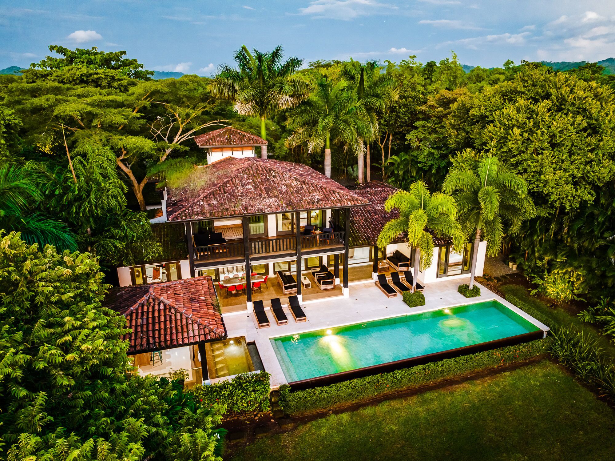 Ein zweistöckiges Haus mit Pool, umgeben von üppigem Grün und Palmen.