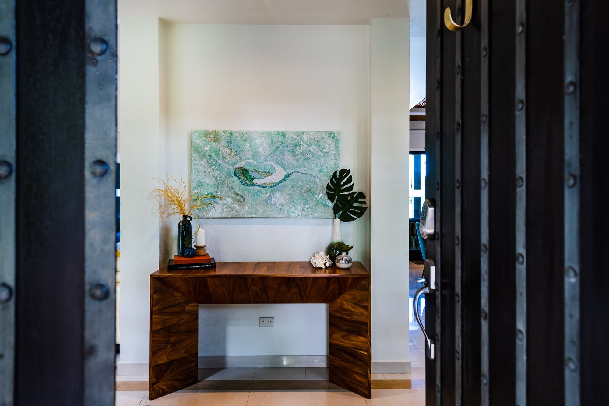 A modern desk with a wooden finish, a green abstract painting on the wall, and a potted plant on the desk.