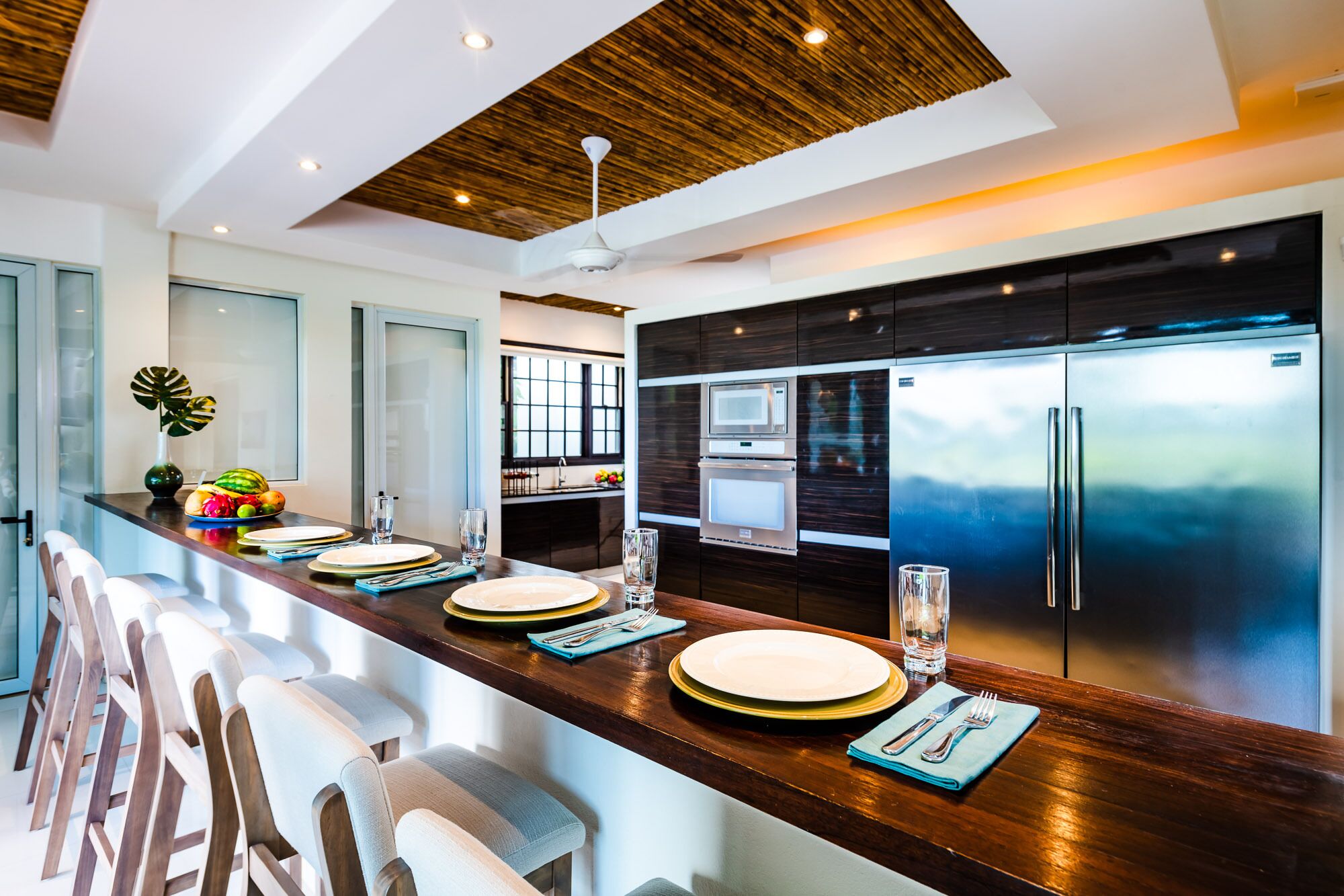 A modern kitchen with a long island, stainless steel appliances, and a wooden ceiling.