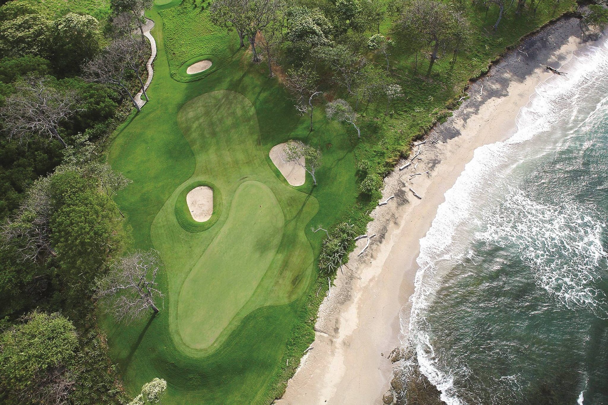 Vista aérea de un campo de golf con una playa y el océano en un lado.