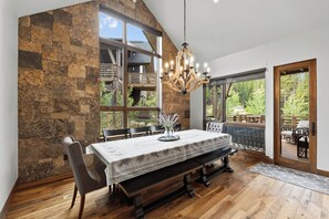 Un comedor con pared de piedra, ventanas amplias y una araña.