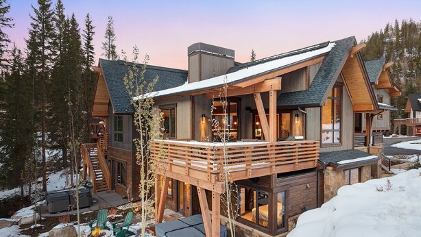 Een houten lodge met een terras, grote ramen en een stenen fundering.