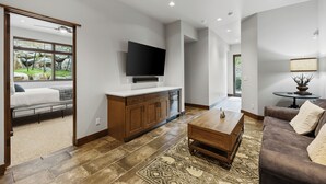 Een moderne woonkamer met een flatscreen televisie, houten kasten, een salontafel en een kamerbreed tapijt met een patroon.