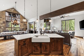 Una cocina amplia con una isla grande, armarios de madera y un comedor con techo alto y vigas a la vista.