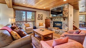 A cozy living room with a stone fireplace, wooden ceiling, and large windows. - Amazing Views | Walk or Free Shuttle to Town (Breckenridge)