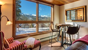 A cozy room with a large window offering a view of snow-covered mountains. There is a table with chairs and a chessboard, and a red-striped sofa. - Amazing Views | Walk or Free Shuttle to Town (Breckenridge)