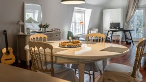 Spiseområde med et rundt bord, fire træstole, en grøn hængende lampe og en guitar i baggrunden.
