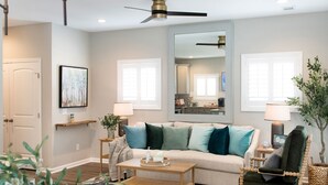 A modern living room with a sofa, coffee table, and chairs. There is a dining table with a vase and a mirror on the wall. - The Jubilee (Northport)