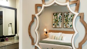 A bedroom with a bed, a mirror, a nightstand, and a vase with flowers. - The Jubilee (Northport)