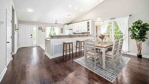 Une cuisine spacieuse avec un coin repas, un plancher en bois et une grande fenêtre agrémentée de rideaux.