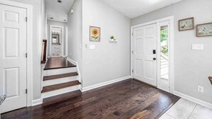 Un couloir doté d’un parquet en bois foncé, de murs blancs et d’une porte blanche au fond.