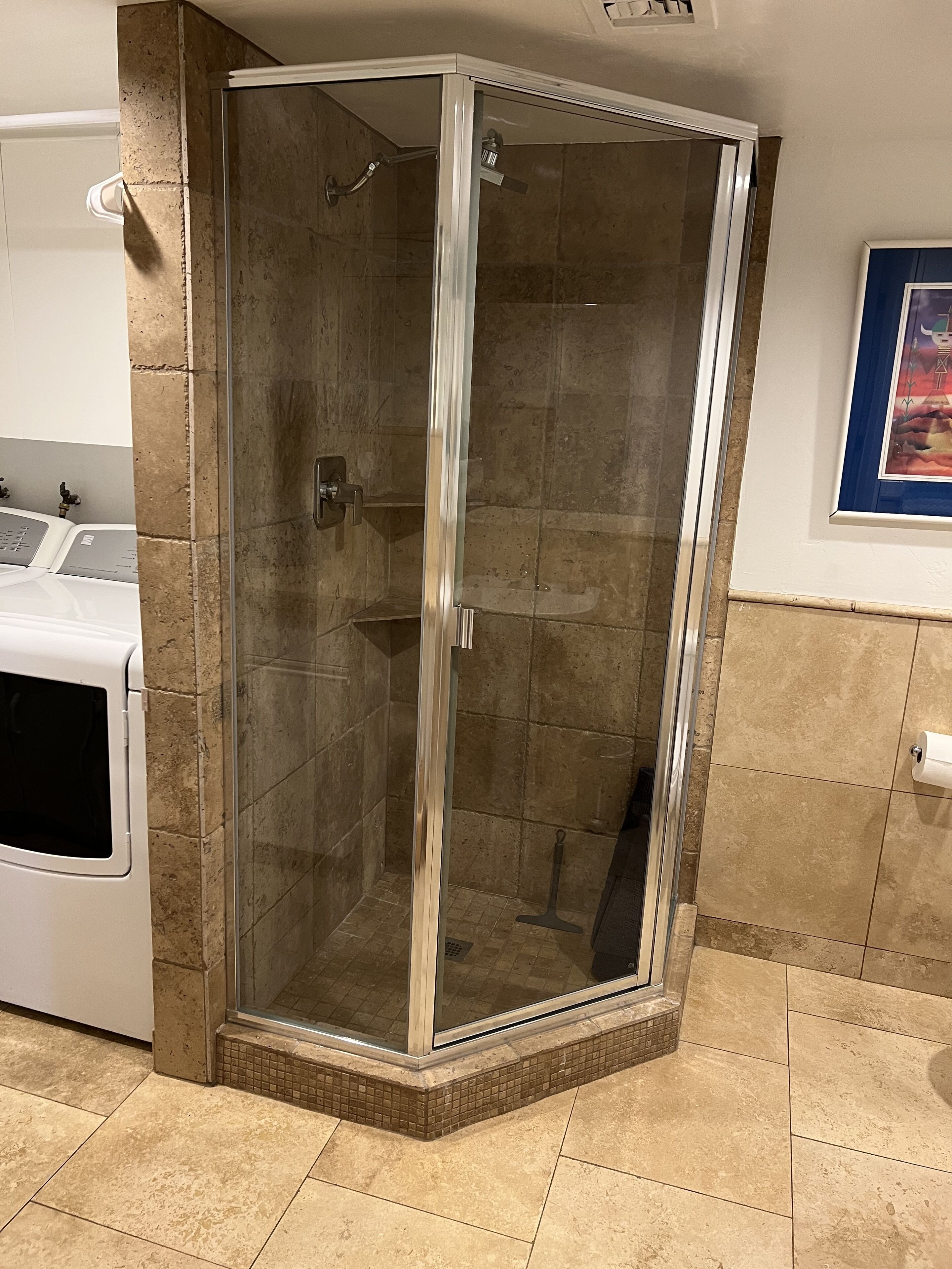 Un espace douche d’angle avec une porte en verre, situé à côté d’un lave-linge et doté d’un sol carrelé.