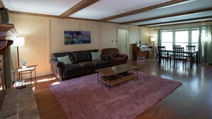 A spacious living room with a wooden floor, a large pink rug, a leather sofa, a coffee table, and a dining area with chairs and a table. - Spacious & Quiet 5 beds, 3.5 bathroom home away from home in Katy, Texas (Katy)