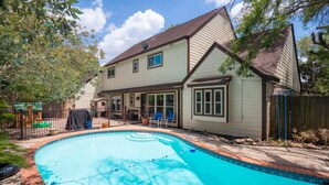 A residential swimming pool with a tiled edge, a covered patio area with chairs, and a house with a gabled roof. - Spacious & Quiet 5 beds, 3.5 bathroom home away from home in Katy, Texas (Katy)