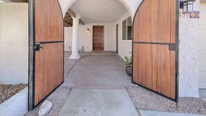 Ein Gebäudeeingang mit zwei Holztüren, einem Betonweg und einer weißen, strukturierten Wand.