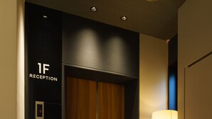A reception area with a wooden door, a digital elevator display, and a standing lamp. - Hotel Sails (Osaka)