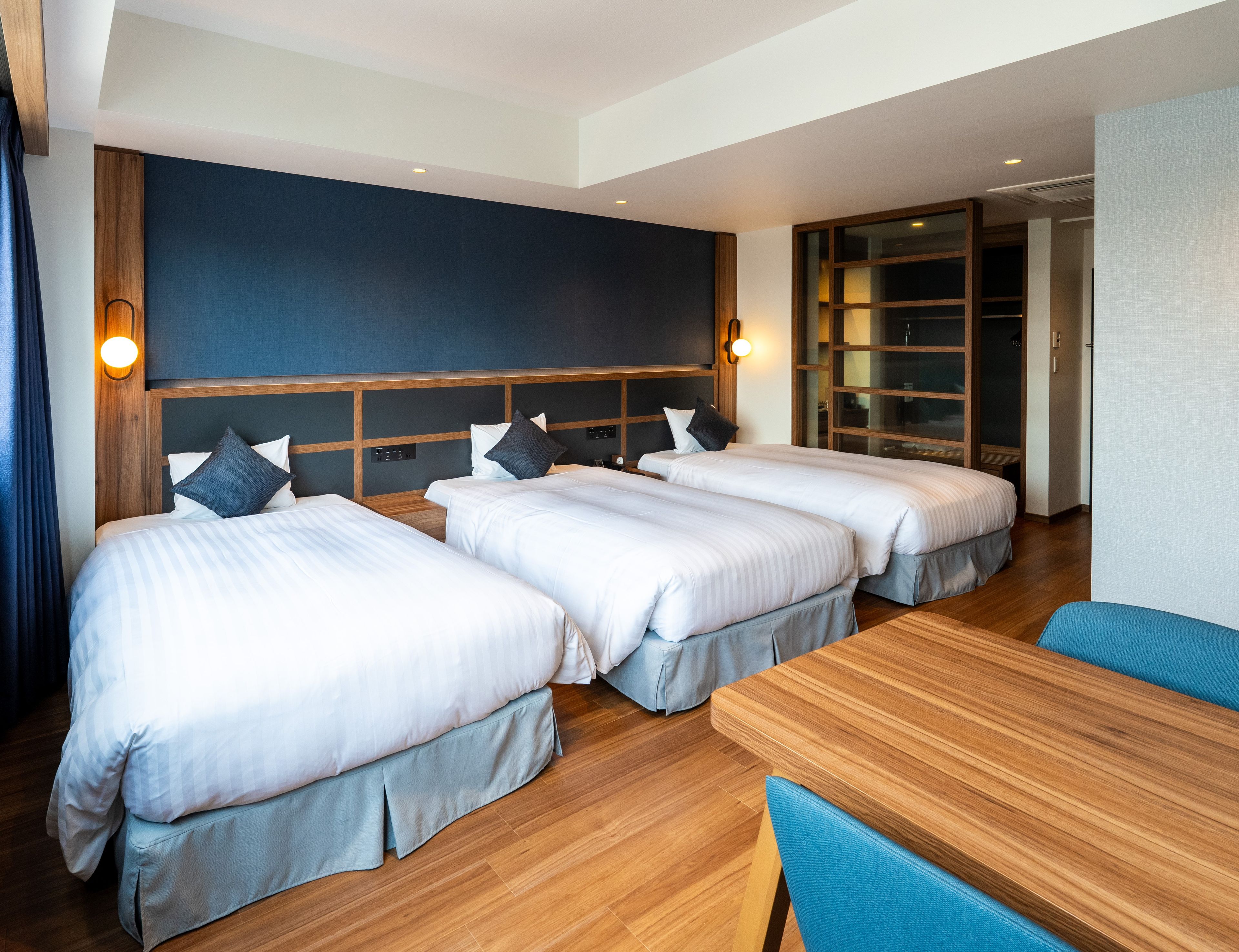 A hotel room with two beds, a wooden headboard, a table, and a blue chair.