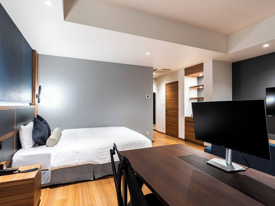 A modern hotel room with a bed, bedside table, desk, and a flat-screen TV.