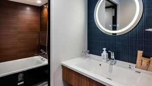 A modern bathroom with a white sink, a mirror with a circular light, and a wooden vanity. - Hotel Sails (Osaka)