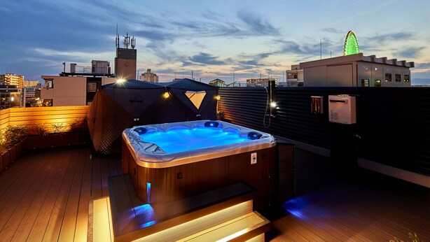 A rooftop with a hot tub, wooden deck, and a Ferris wheel in the background.
