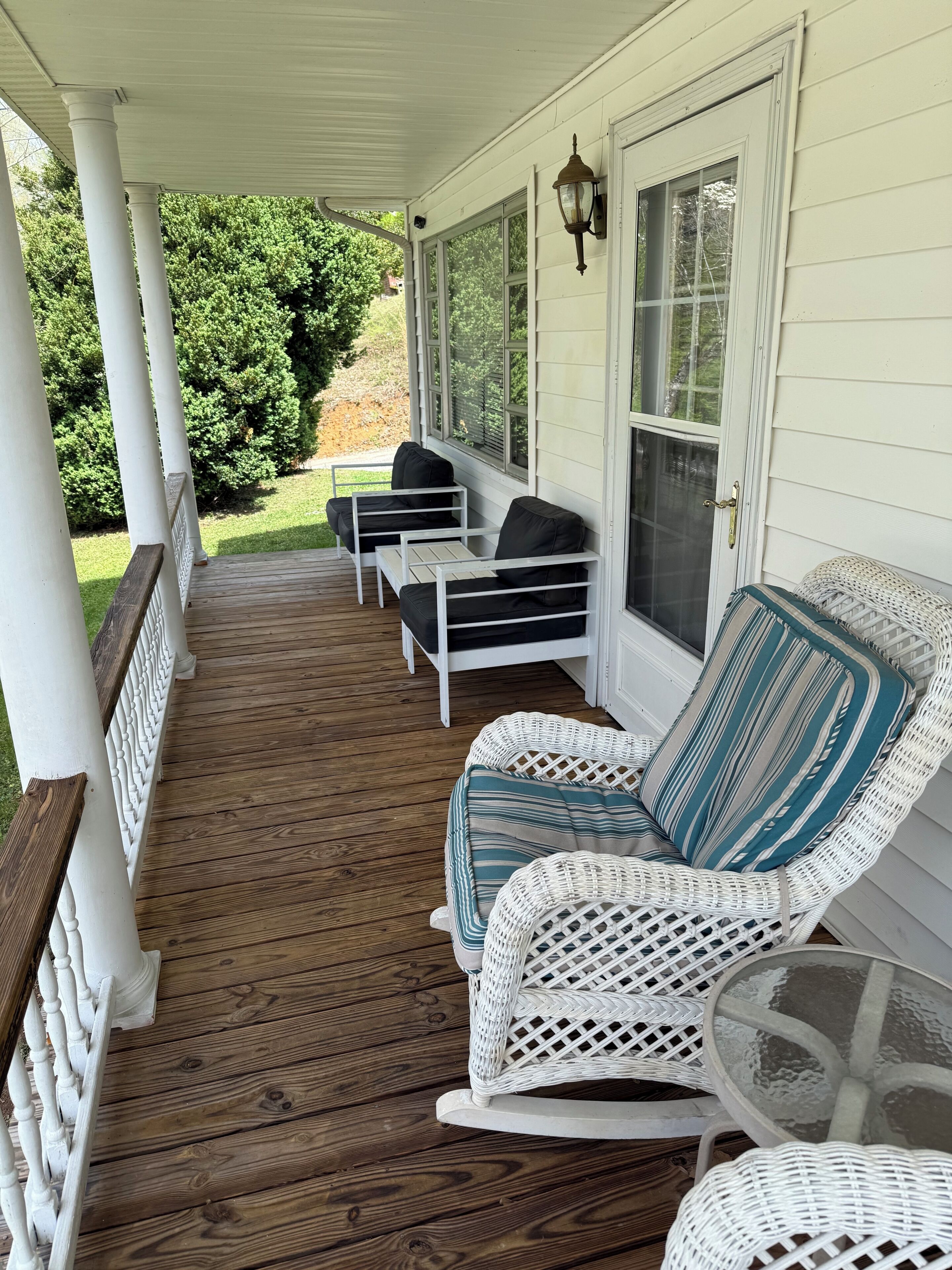 A porch with white wicker furniture, a glass table, and a view of a green landscape.