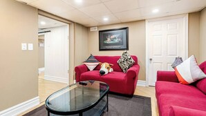 A living room with a red sofa, a glass coffee table, and a framed artwork on the wall. - The Rustic Barn - Urban Retreat | King bed | Pet friendly | Full apartment (Brampton)