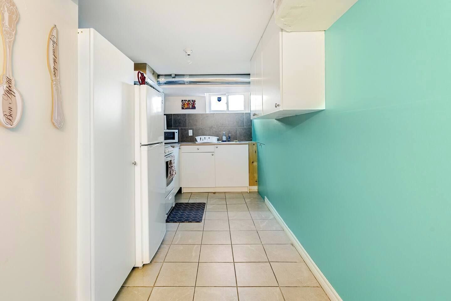 A narrow kitchen with white cabinets, a microwave, and a sink.