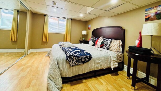 A hotel room with a bed, bedside table, lamp, and a painting on the wall. - The Rustic Barn - Urban Retreat | King bed | Pet friendly | Full apartment (Brampton)