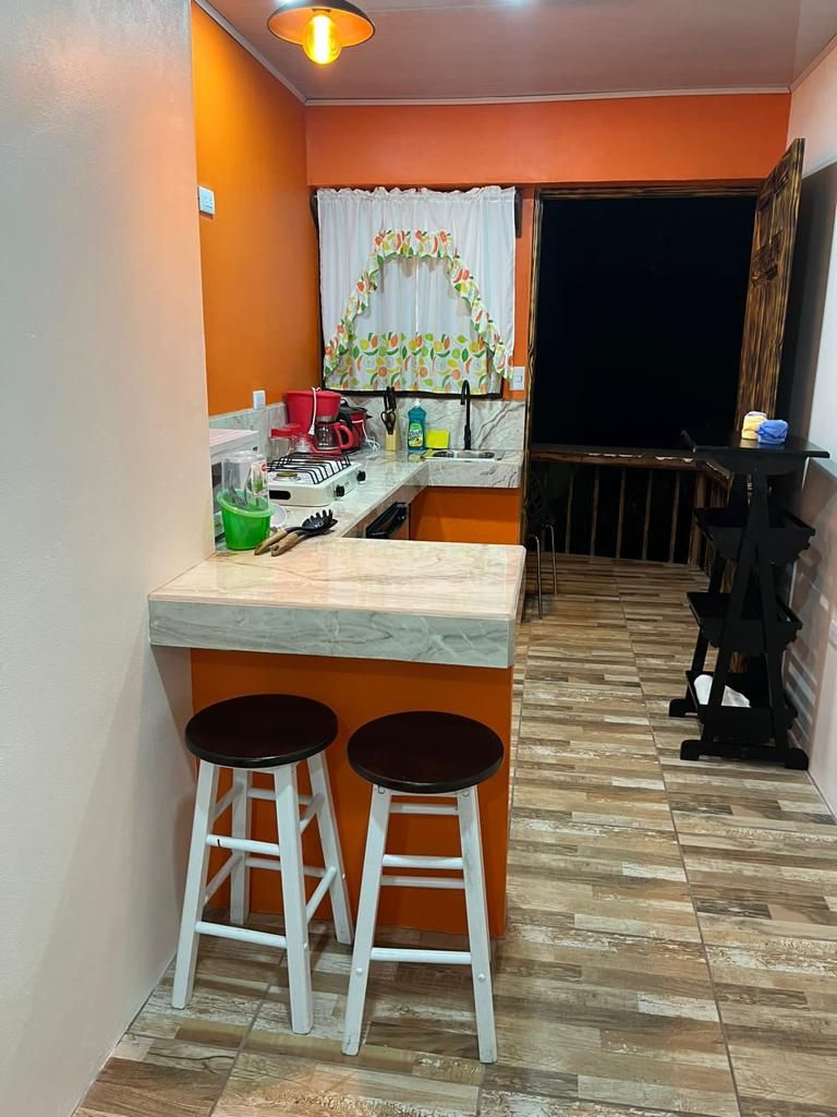 A compact kitchen with a marble countertop, two stools, and a wooden floor.