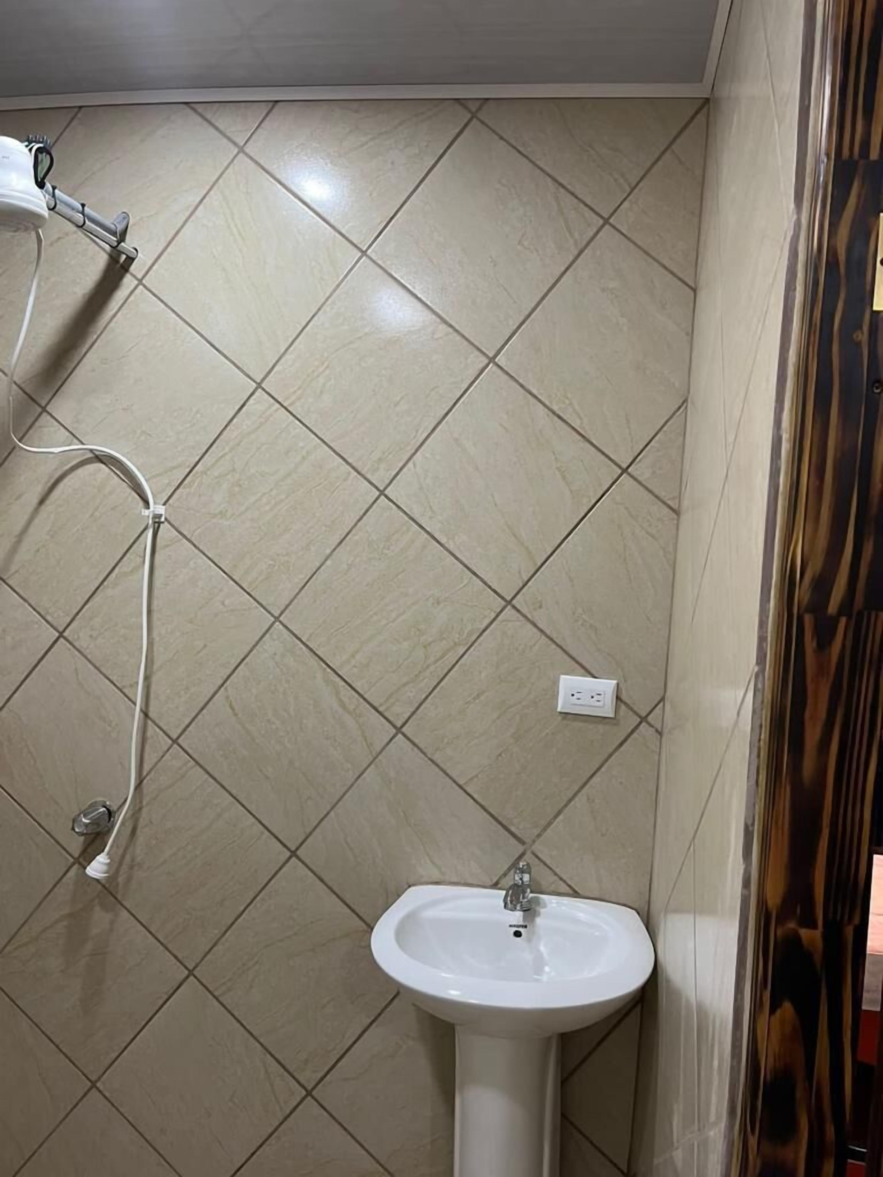 Een badkamer met een witte wastafel, een douche met een handdouche en betegelde wanden.