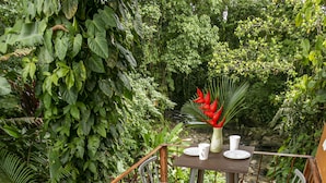 A wooden deck with a table and chairs surrounded by lush greenery.