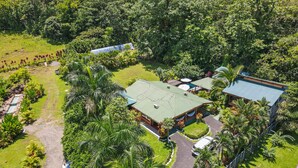 An aerial view of a resort with a central building surrounded by lush greenery, a swimming pool, and a covered outdoor area.