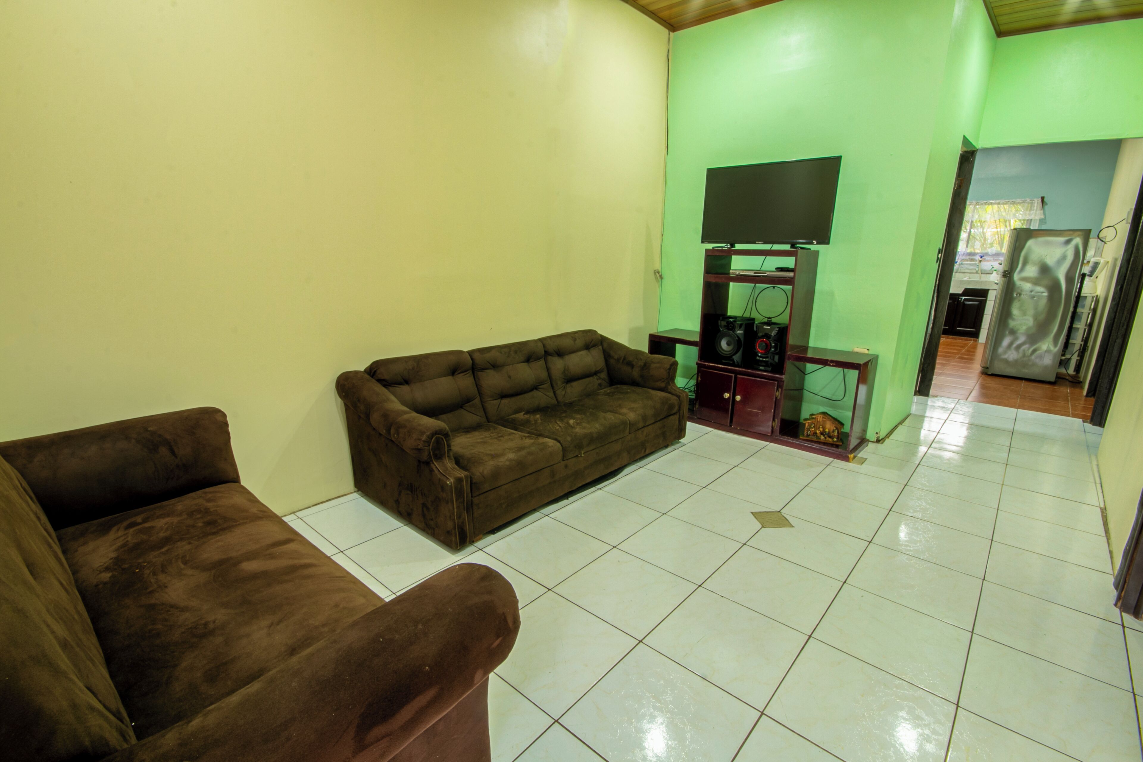 A living room with a brown sofa, a television on a stand, and a tiled floor.