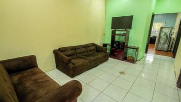 A living room with a brown sofa, a television on a stand, and a tiled floor.