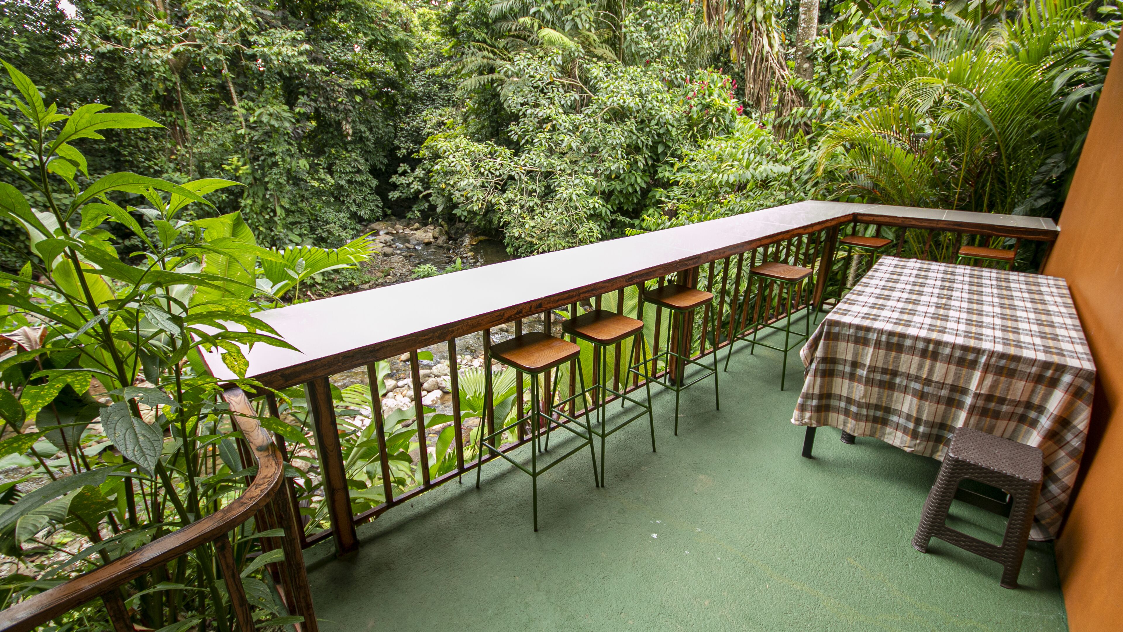 A balcony with a table and bar stools, surrounded by lush greenery.