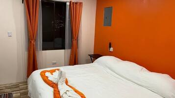 Een hotelkamer met een bed, oranje gordijnen, een raam en een wandlamp-schakelaar.