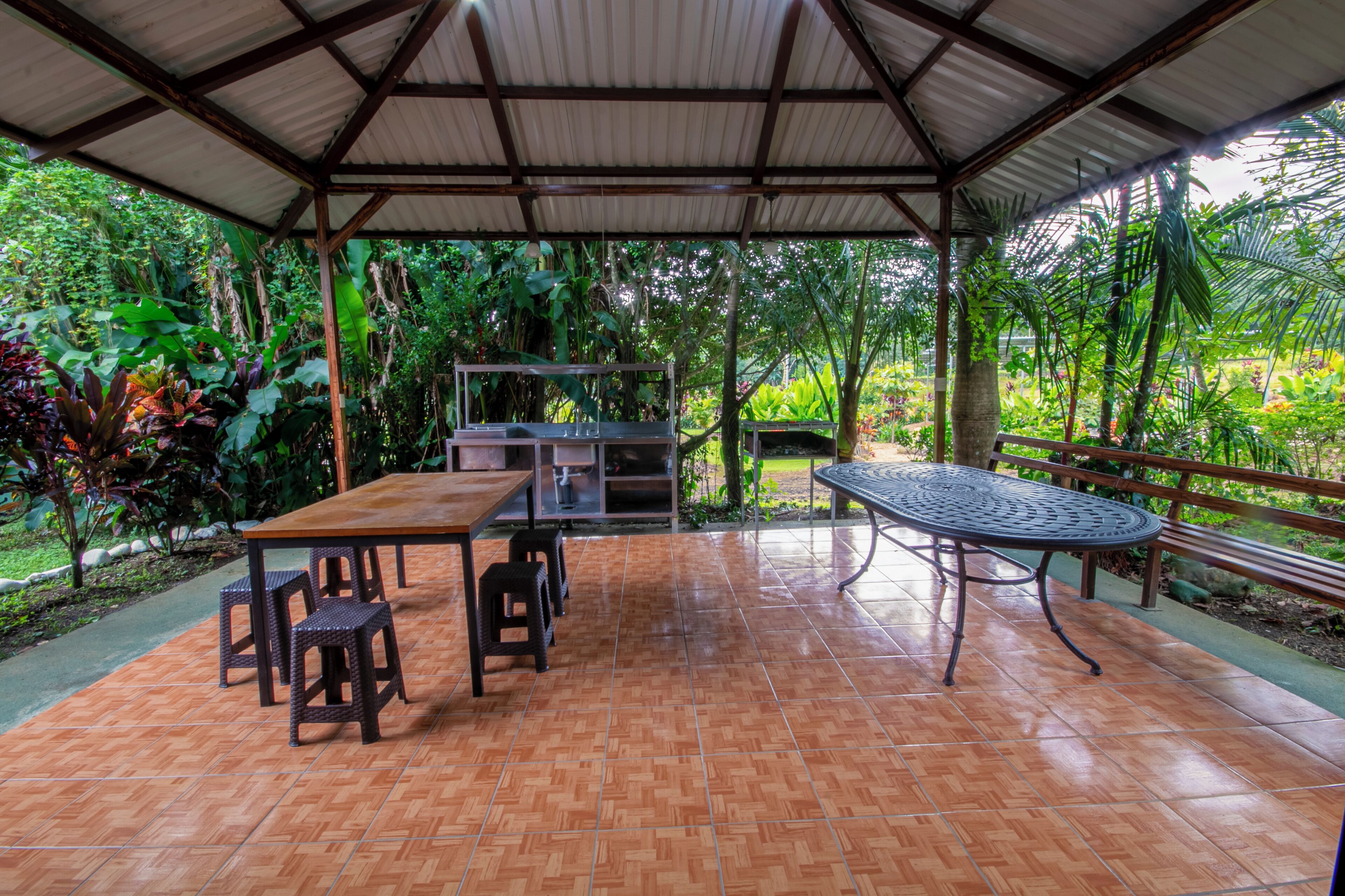 An outdoor patio with a wooden table and chairs, a metal table, and a grill.