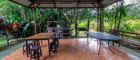 Un patio exterior con una mesa y sillas de madera, una mesa de metal y una parrilla.