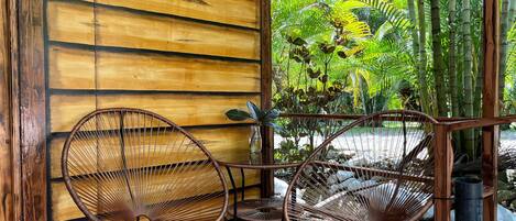 Un interior de madera con dos sillones de mimbre y una mesita, una pared de madera y vistas a un follaje exuberante.