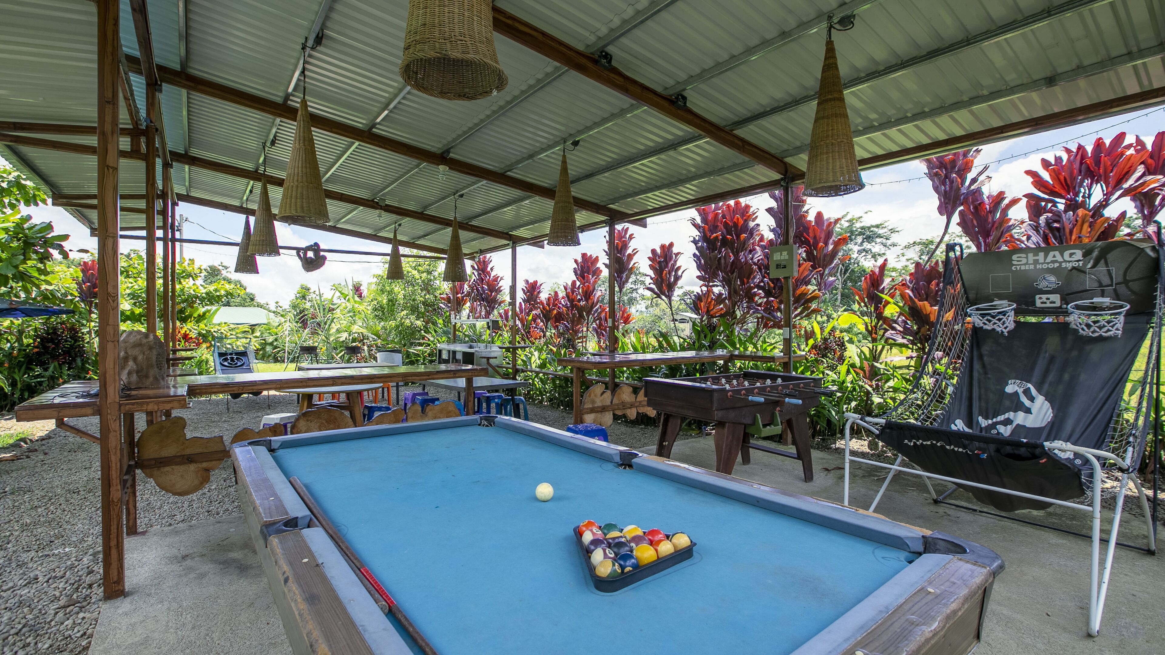 An outdoor pool area with a blue pool table, foosball table, and a cyber hoop.