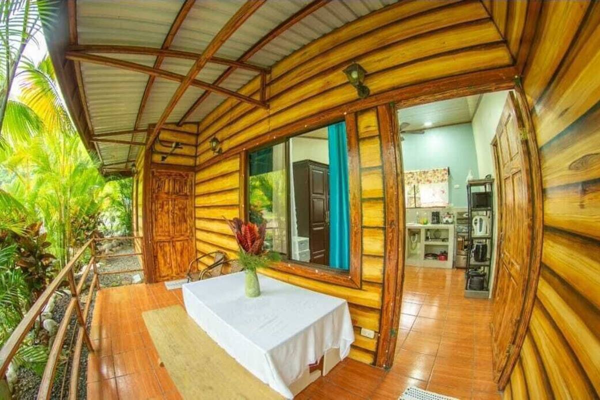 Una baita in legno con zona pranzo, tavolo e sedie, angolo cottura e vista sul verde circostante.