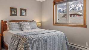 A bedroom with a large bed, a window with a mountain view, and two framed pictures on the wall. - APEX Magnificent mountain view condo Pool &Hot Tub (Canmore)