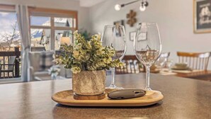 A dining area with a wooden table, a potted plant, two wine glasses, and a remote control. - APEX Magnificent mountain view condo Pool &Hot Tub (Canmore)
