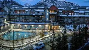 A multi-story hotel with a pool area, surrounded by snow-covered mountains. - APEX Magnificent mountain view condo Pool &Hot Tub (Canmore)