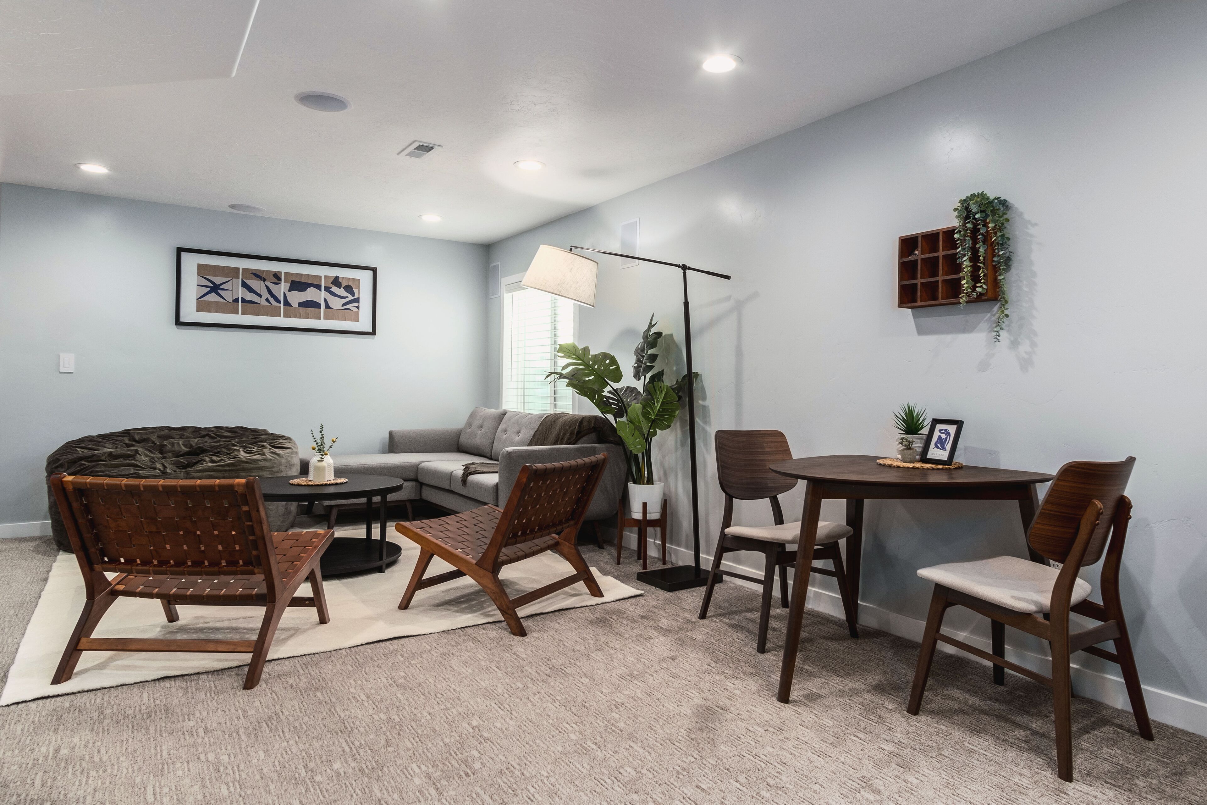 Un salon moderne comprenant un canapé, deux fauteuils, une table basse et une table à manger avec des chaises. On y trouve également un lampadaire, une plante en pot et un tableau encadré accroché au mur.
