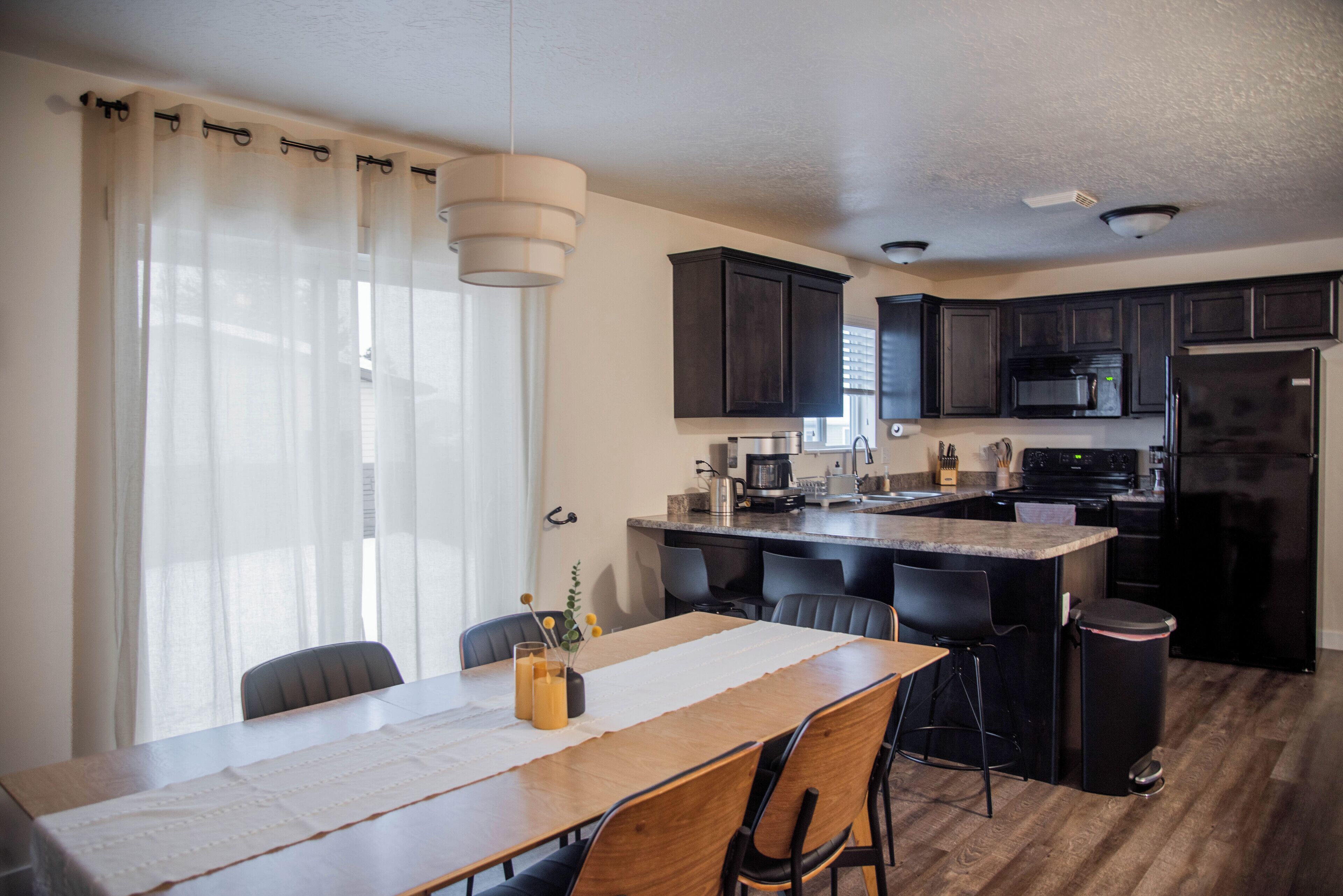 A modern kitchen with dark cabinets, a central island, and a dining area with a table and chairs.