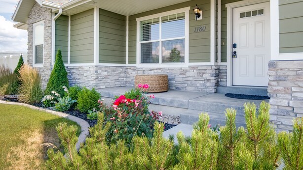 A house with a stone facade, a front porch, and a well-maintained garden with various plants and flowers.